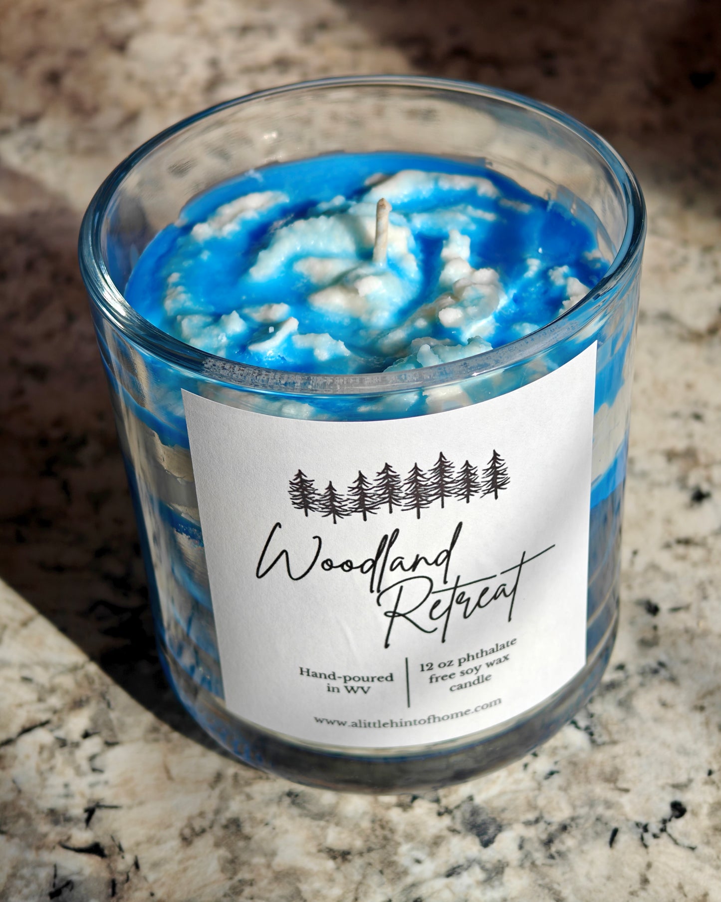 Candle with blue and white design in a glass jar on a marble surface, labeled 'Woodland Retreat'.