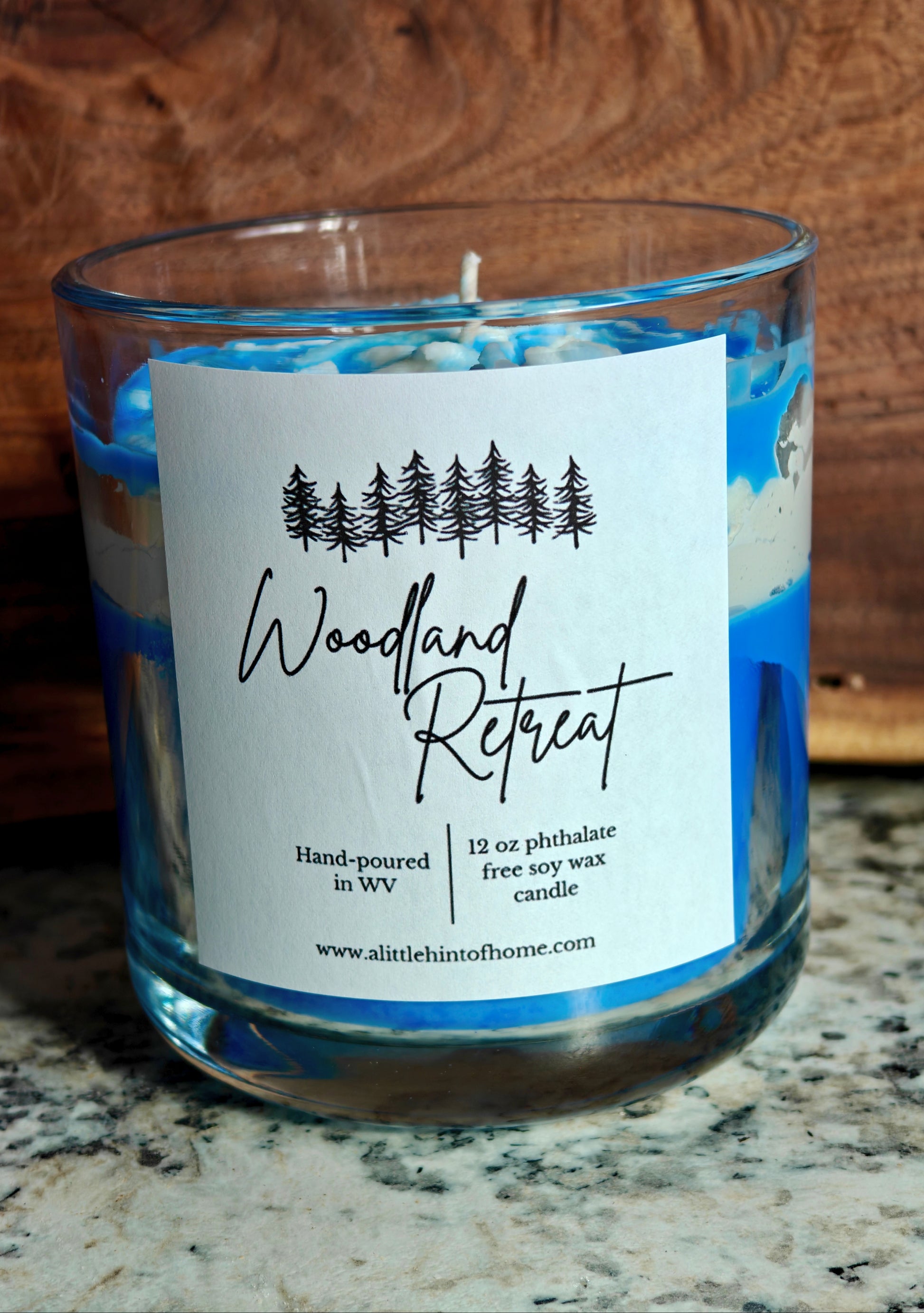 Candle with blue and white design in a glass jar on a marble surface, labeled 'Woodland Retreat'